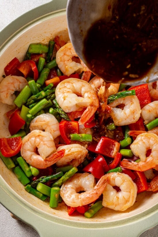 Stir fry sauce being poured over shrimp, asparagus, and red bell peppers